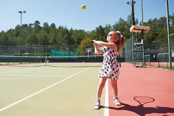 Happy little girl playing tennis summer sport